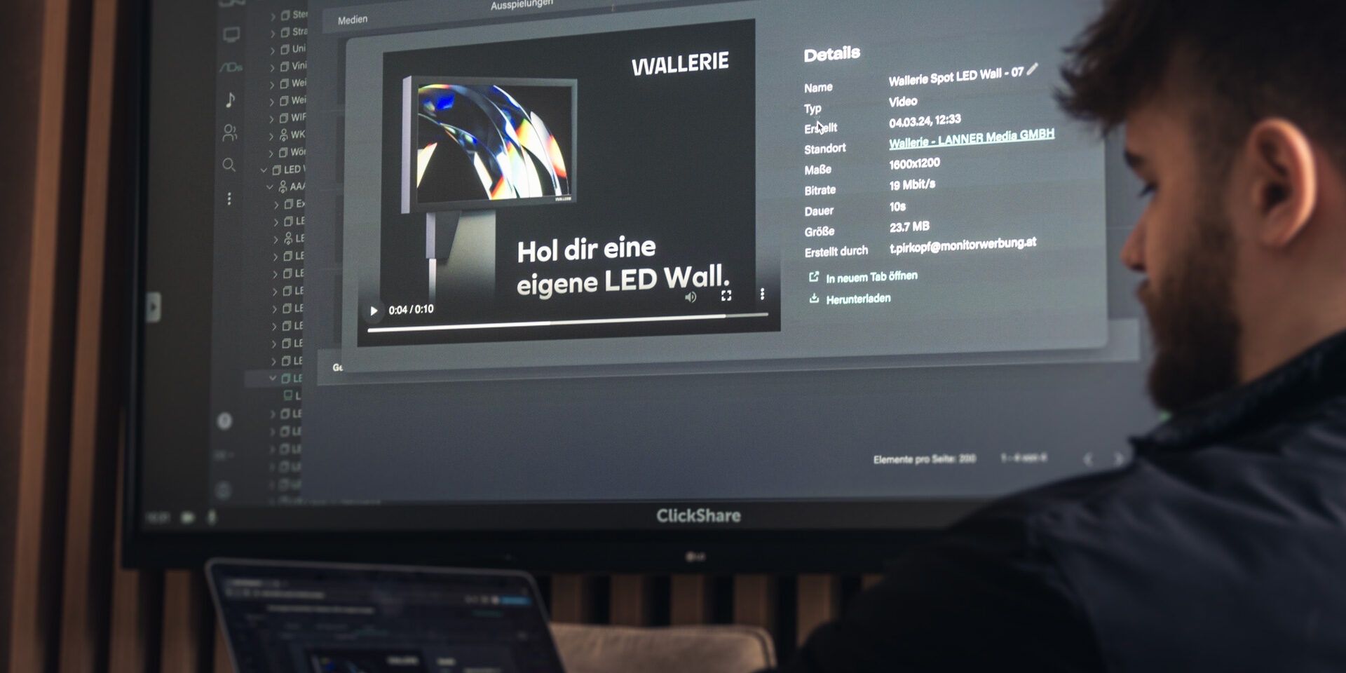 Foto von Mitarbeiter Pascale Lercher vor einem Laptop und Meeting-Raum-Monitor mit dem Content Management System von Wallerie