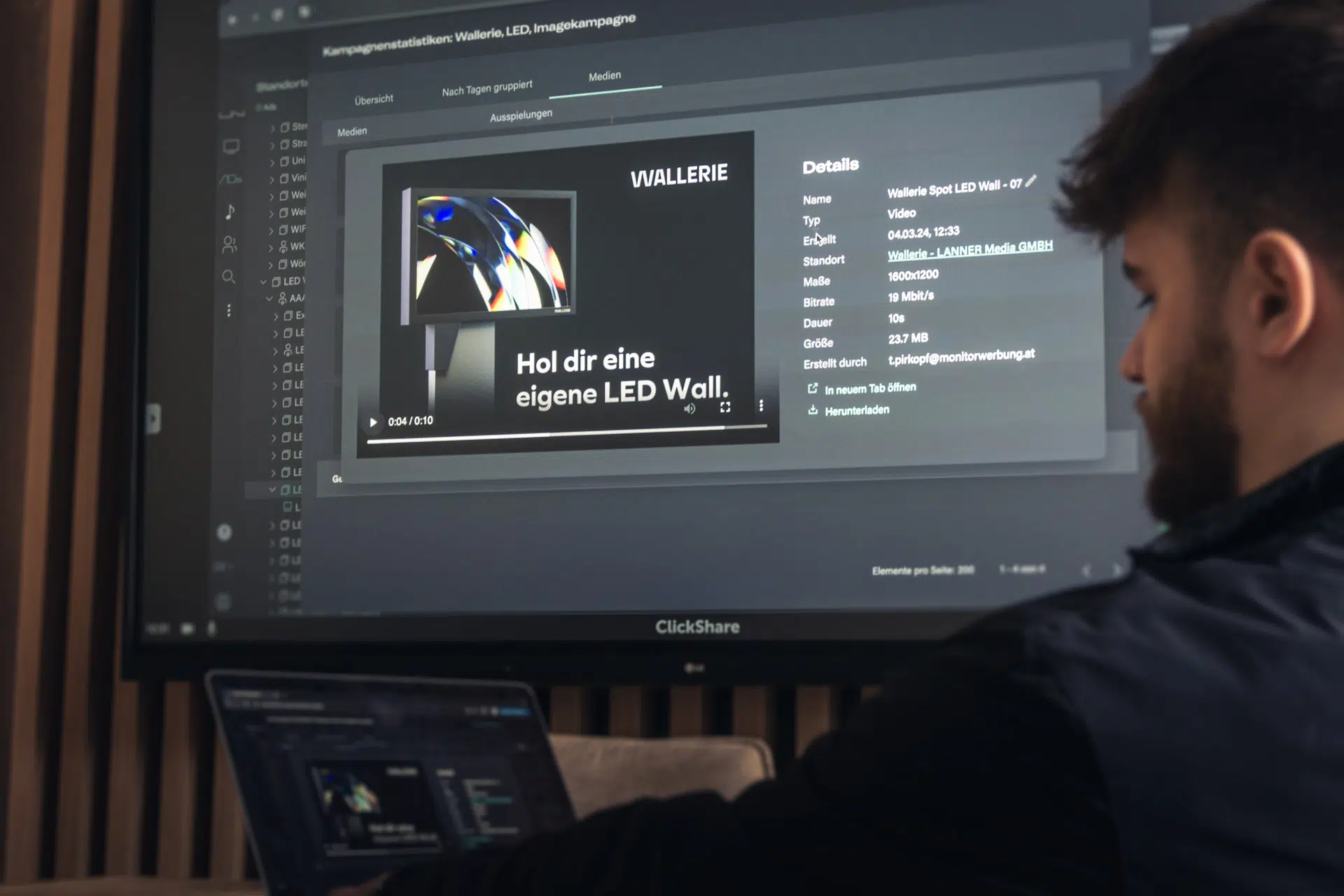 Foto von Mitarbeiter Pascale Lercher vor einem Laptop und Meeting-Raum-Monitor mit dem Content Management System von Wallerie