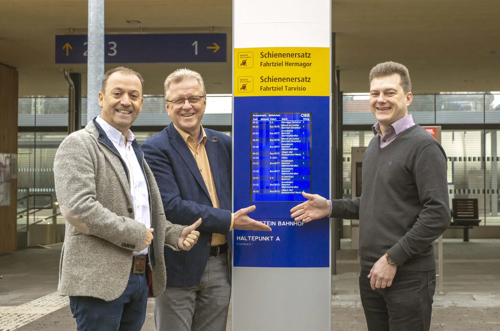 Foto von Andreas Lanner (Geschäftsführer Lanner Media Group), Bürgermeister Reinhard Antolitsch und Herwig Steiner (ÖBB-Projektkoordinator Koralmbahn 2) präsentieren den neuen Echtzeit-Screen am Bahnhof Arnoldstein.