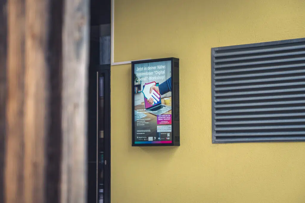 Ein Outdoor Screen hängend an einer gelben Wand vor einem Gebäude.