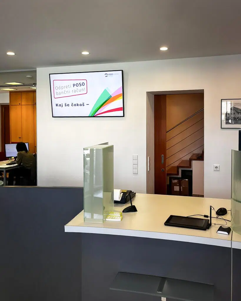 poso-bank-managed-digital-signage-system-by-wallerie-03 Digital Signage Screen an der Wand einer Posojilnica Bank-Filiale: Werbeslide mit dem Aufruf, ein POSO-Bankkonto zu eröffnen, mit bunten Farbstreifen im Corporate Design.