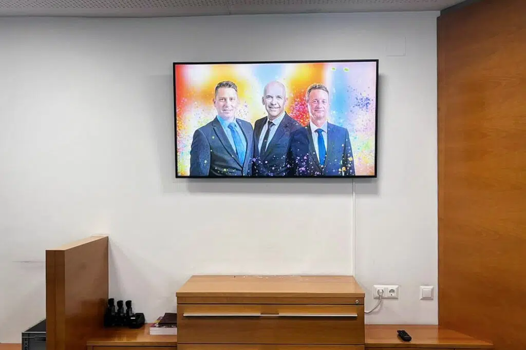 poso-bank-managed-digital-signage-system-by-wallerie-05 Digital Signage Screen in einem Beratungsraum der Posojilnica Bank: Porträt von drei Männern in Businesskleidung vor einem farbenfrohen, dynamischen Hintergrund.
